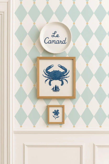 a wall with a diamond pattern wallpaper, a white plate with the word "Camard" written on it, and two framed pictures hanging on the wall.
