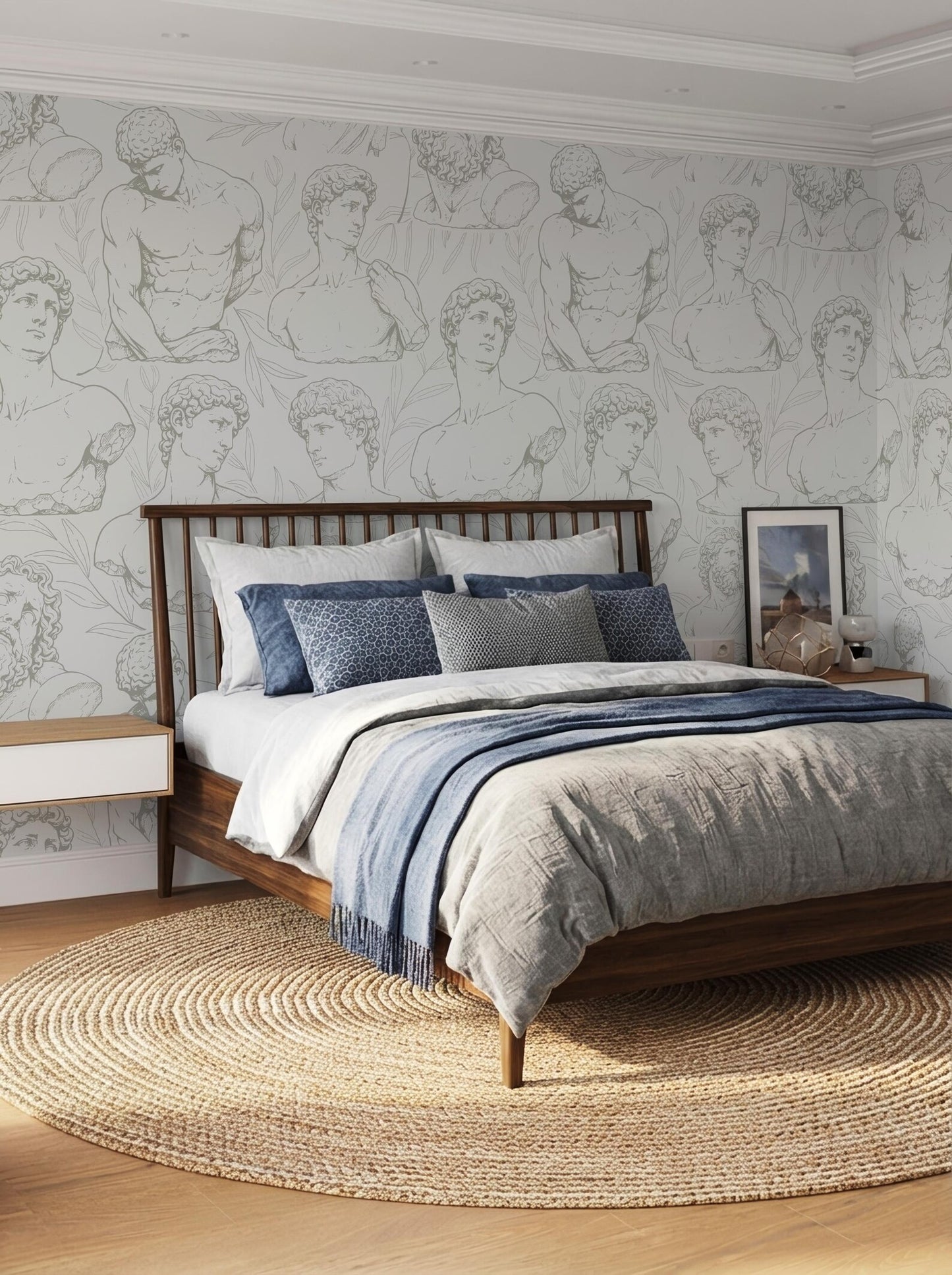 a bedroom with a large bed, a wooden headboard, and a patterned wallpaper with multiple human figures. The bed is dressed in a gray comforter and blue pillows. The room has a round rug on the floor, and there is a framed picture on the wall.