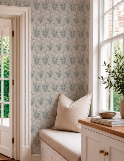 a cozy corner of a room with a window, a white cabinet, and a beige pillow on a bench. The wall behind the bench has a repeating pattern of green and white flowers, creating a visually appealing and harmonious design.