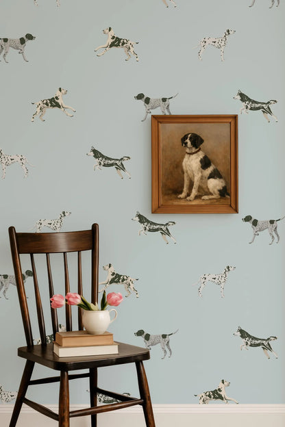 a wooden chair with a vase of pink flowers and a stack of books on it, set against a wall with a framed painting of a dog.