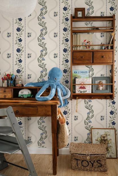 a cozy and well-organized room with a wooden desk, a bookshelf, and a stuffed octopus toy. The room has a floral wallpaper pattern and a wooden shelf with various items on it.