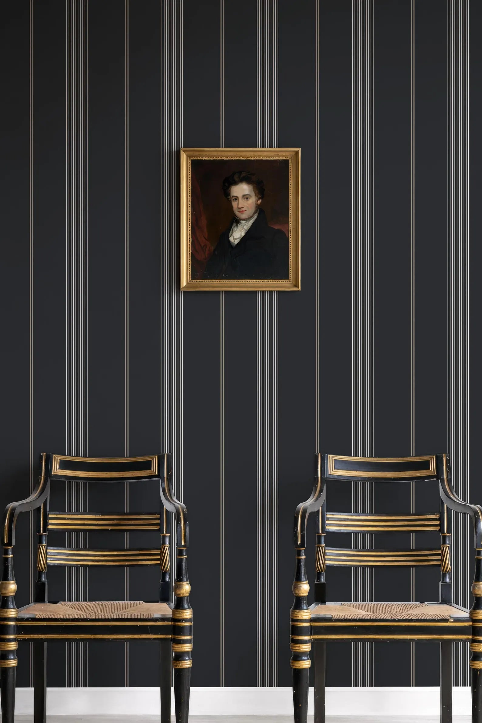 two ornate chairs with gold accents, set against a dark striped wall with a framed portrait hanging above them.