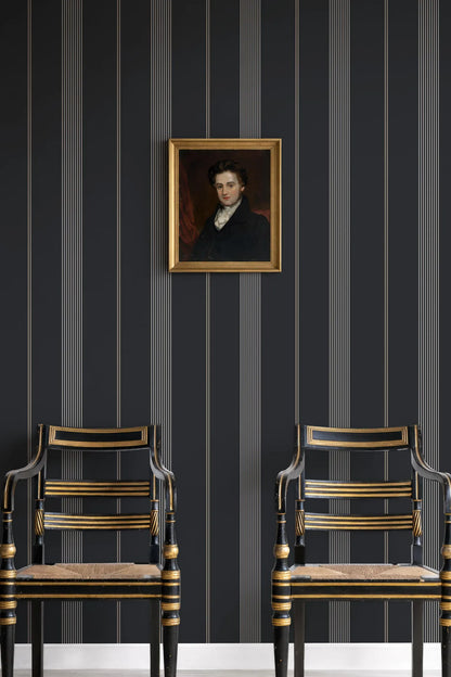 two ornate chairs with gold accents, set against a dark striped wall with a framed portrait hanging above them.