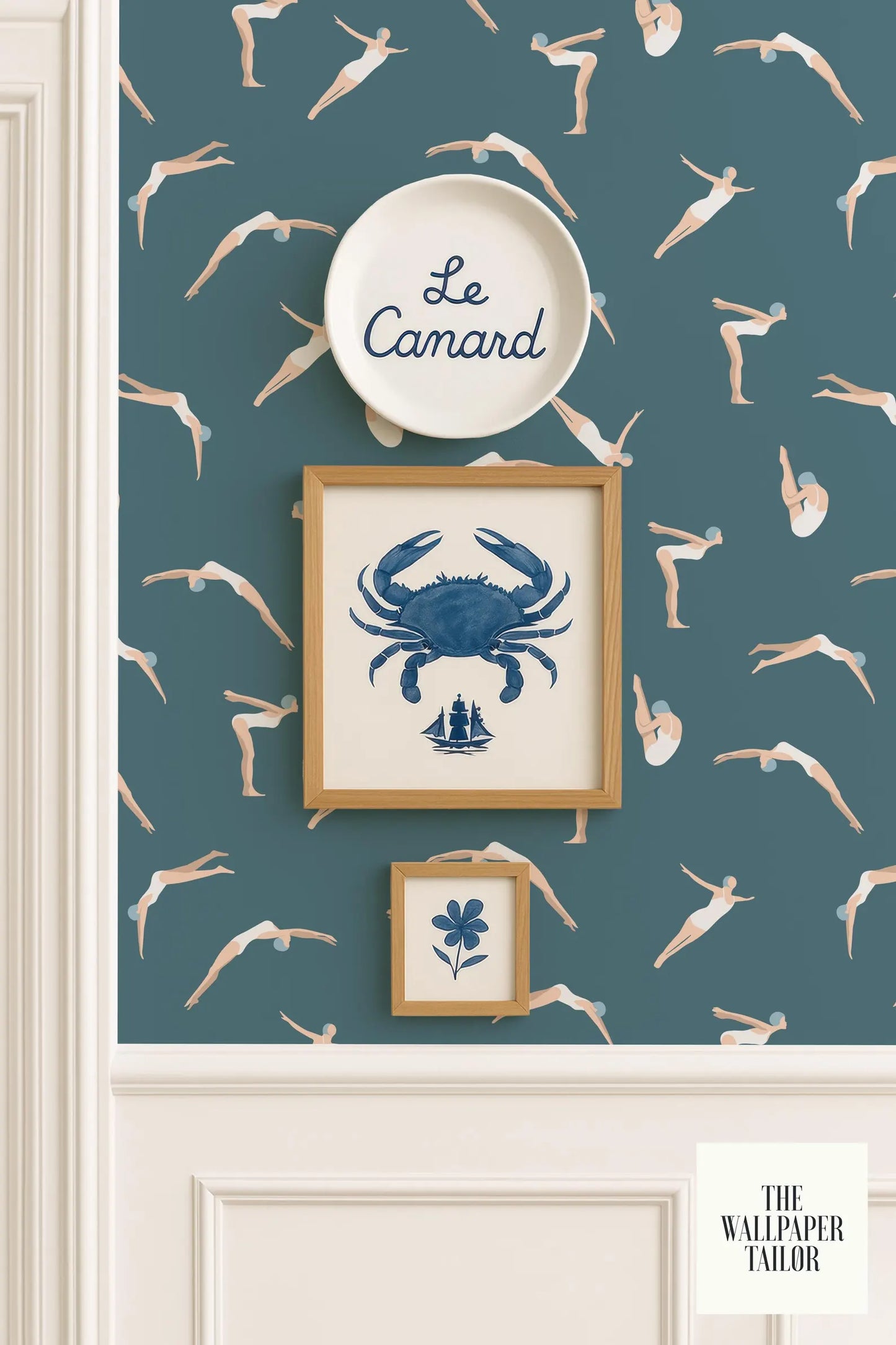 a wallpapered wall with a framed picture of a crab, a framed picture of a flower, and a framed picture of a person diving. The wallpapered wall has a pattern of swimming figures, and there is a plate with the word "Camard" written on it.