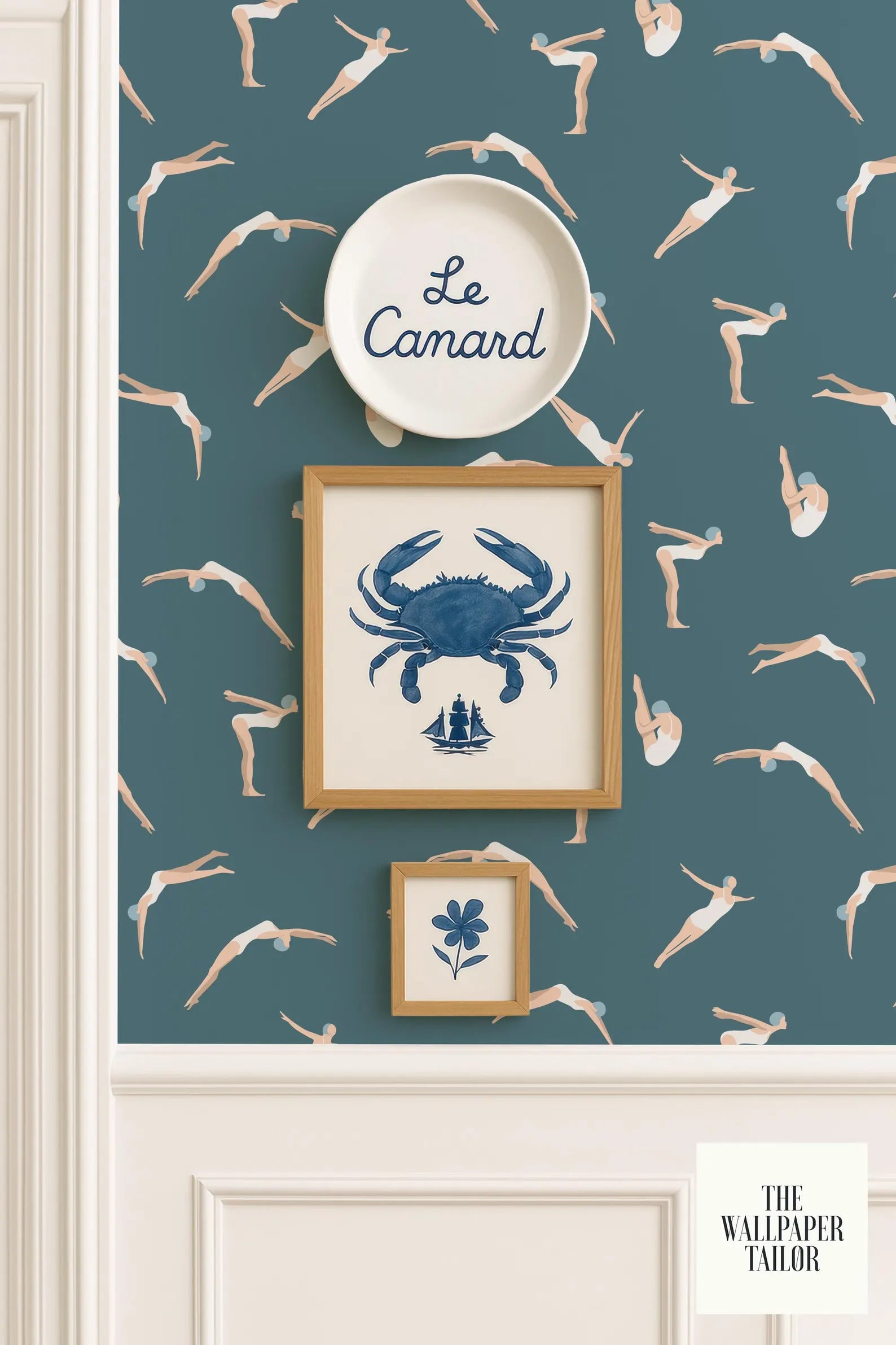 a wallpapered wall with a framed picture of a crab, a framed picture of a flower, and a framed picture of a person diving. The wallpapered wall has a pattern of swimming figures, and there is a plate with the word "Camard" written on it.
