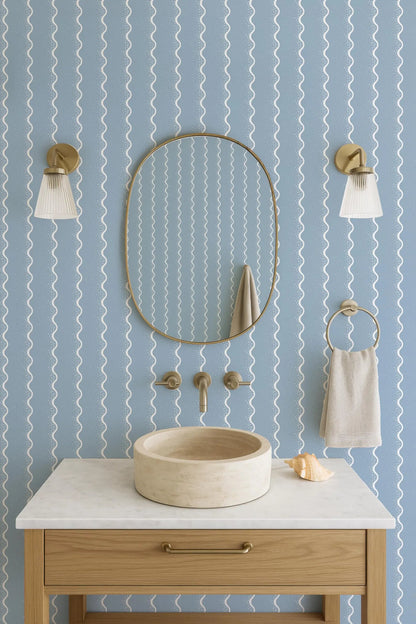 a bathroom with a white marble sink, a round mirror, and two wall sconces. The walls are covered in a blue and white striped pattern, creating a modern and stylish atmosphere.