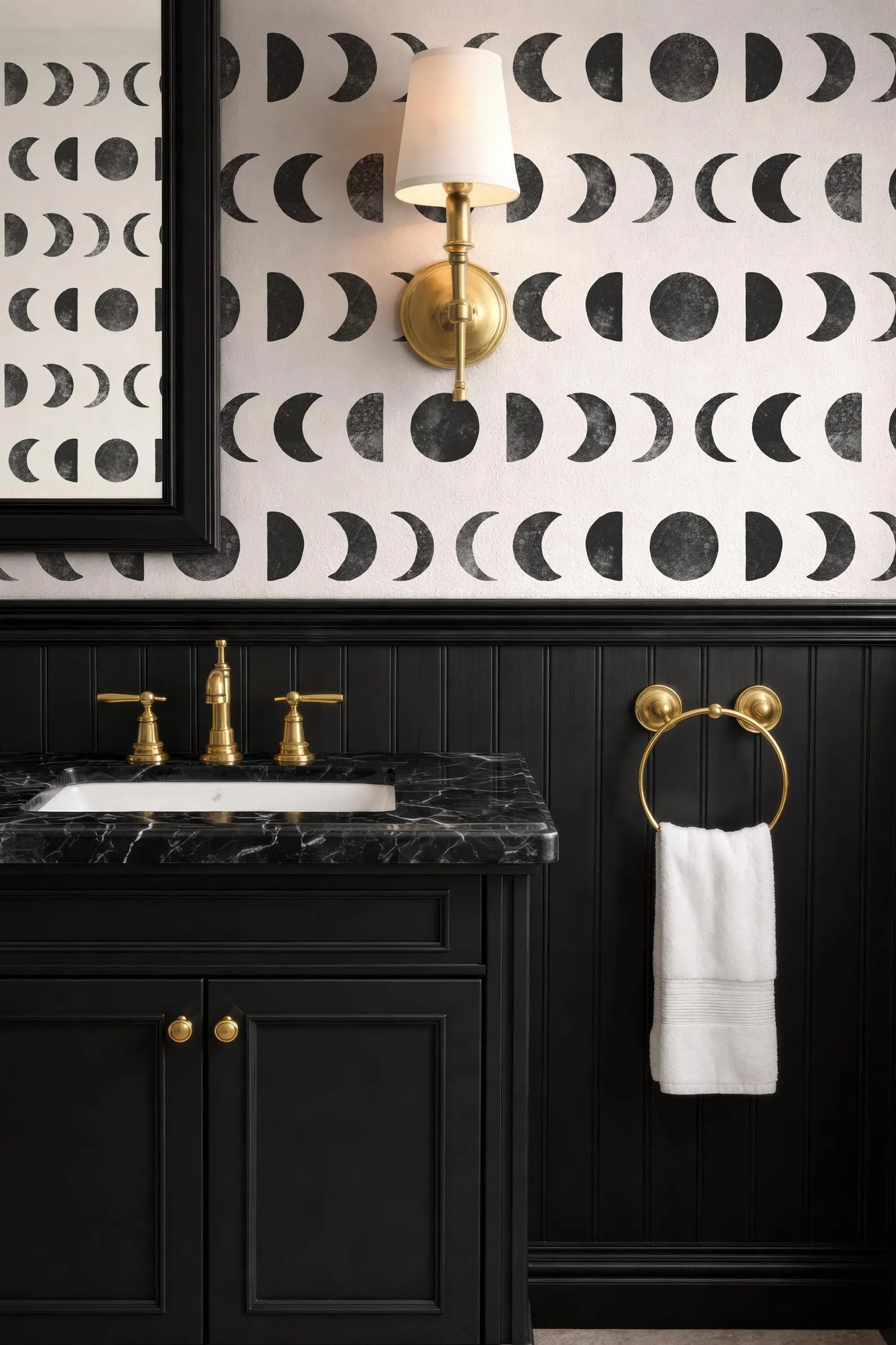 a bathroom with a black and white patterned wallpaper, a black vanity with gold fixtures, and a white towel hanging on a gold towel ring.