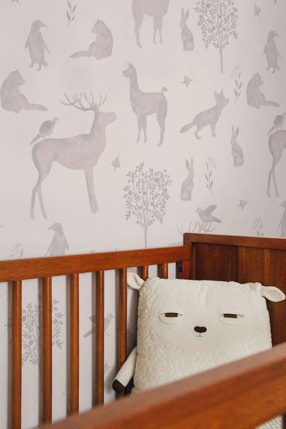 a wooden crib with a white sheep-shaped pillow on it, set against a wall with a repeating pattern of animal silhouettes.