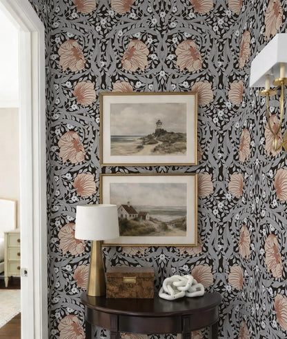 a corner of a room with a dark wood table, a lamp, and two framed paintings hanging on the wall above it. The wall is covered in a floral patterned wallpaper, and the overall color scheme is a combination of black, white, and orange.