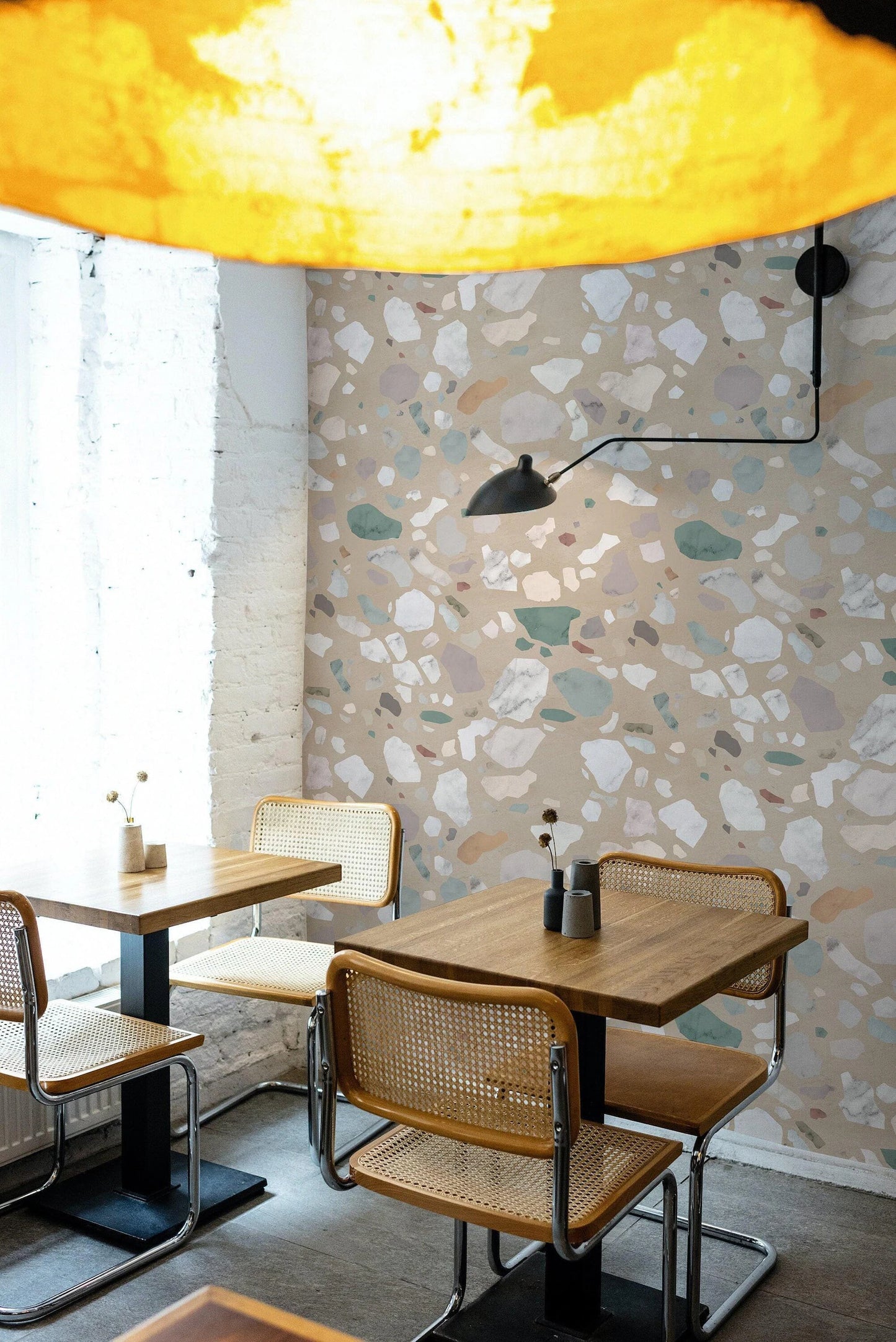 a modern dining area with a wooden table and chairs, a large yellow lamp, and a patterned wall behind the table.