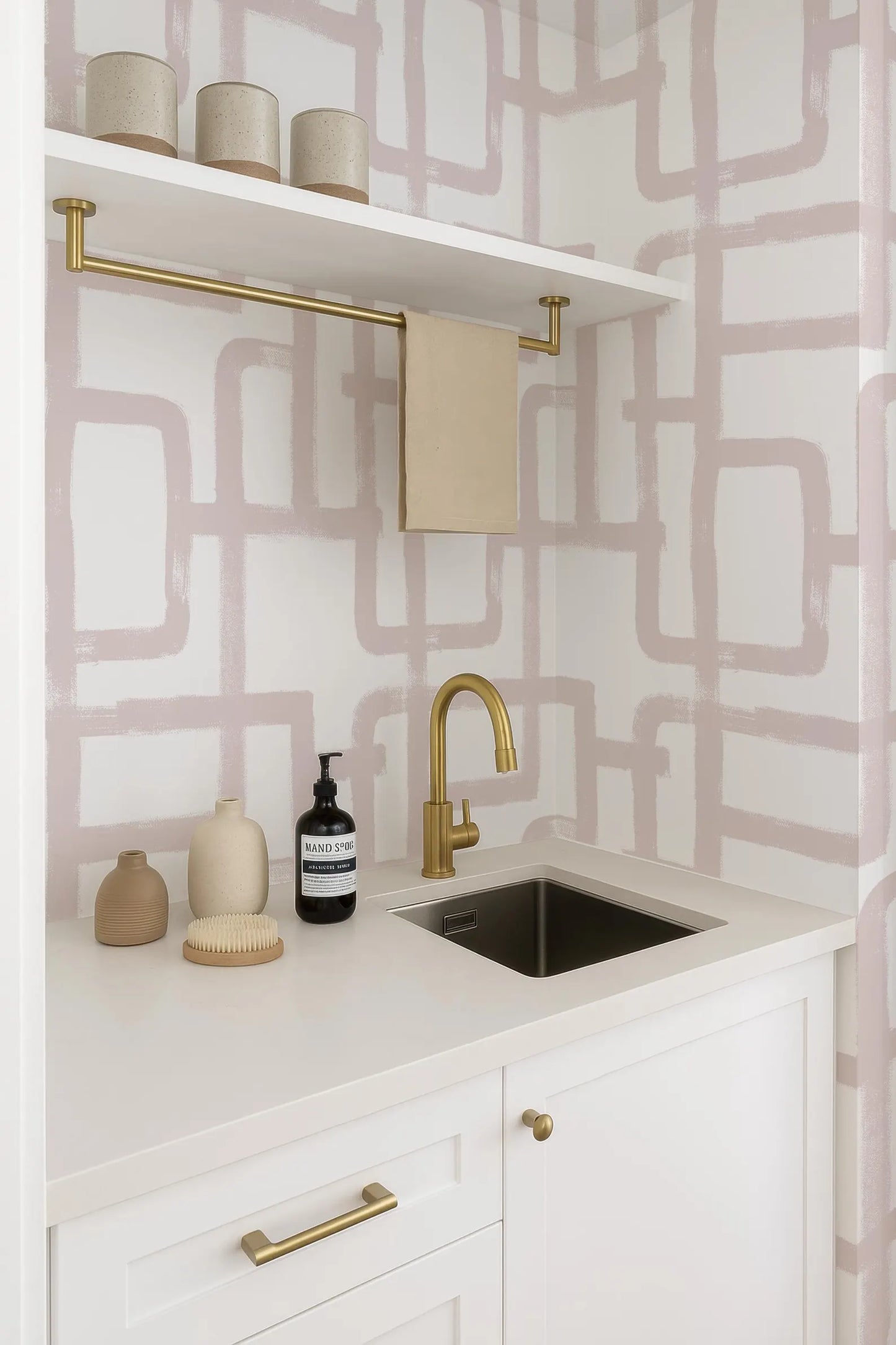 a bathroom with a white countertop, a sink, and a shelf with decorative items. The wall behind the countertop has a geometric pattern in shades of pink and white.