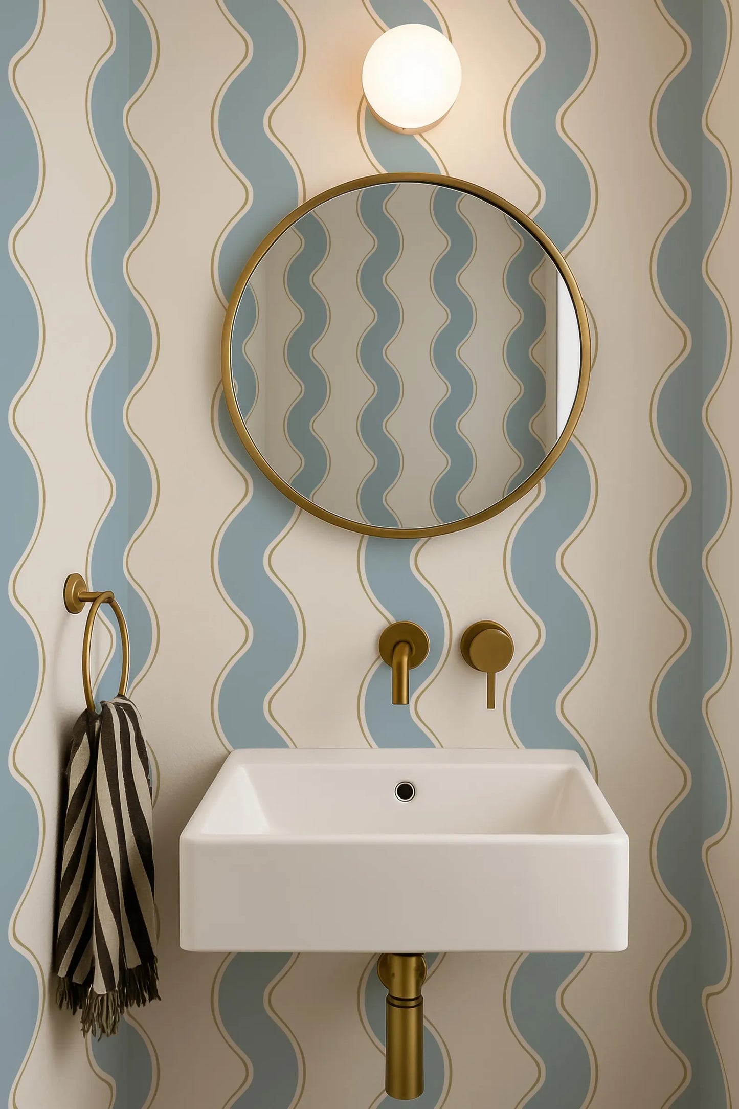 a bathroom with a white sink, a round mirror, and a striped towel. The walls are covered in blue and white wavy wallpaper, creating a modern and stylish atmosphere.