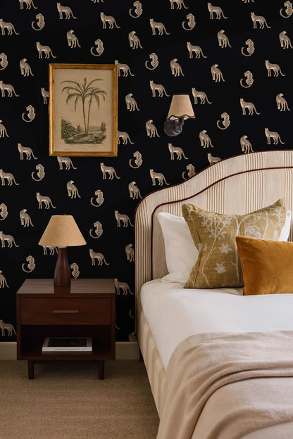 a bedroom with a black and white wallpaper pattern featuring a repeating design of cats. The room includes a bed with white linens, a wooden nightstand with a lamp, and a framed picture on the wall.