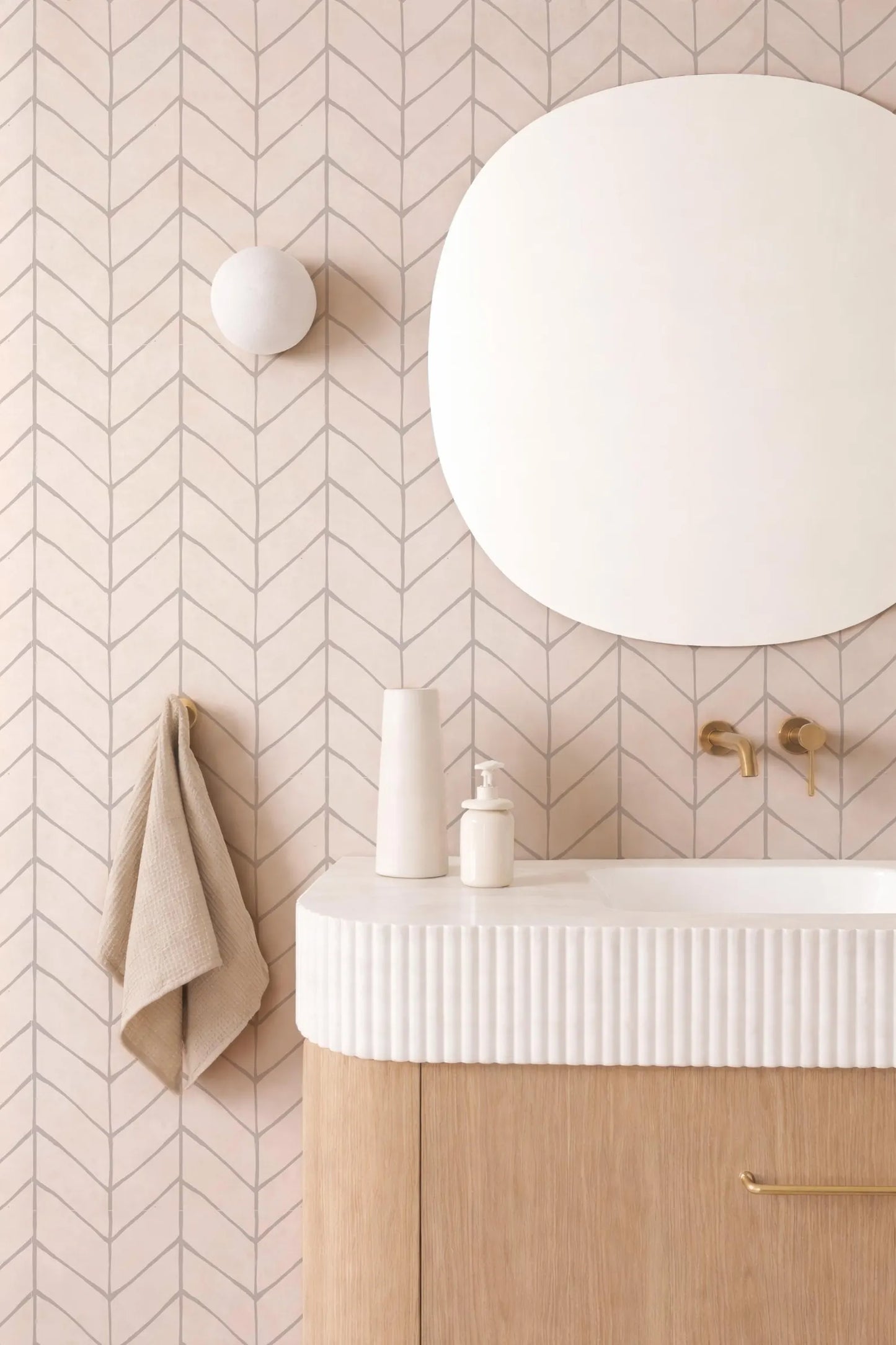 a bathroom with a white sink, a round mirror, and a beige towel hanging on the wall. The bathroom has a chevron patterned wall, and the overall color scheme is predominantly white and beige.