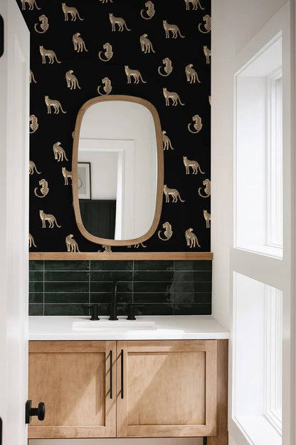 a bathroom with a black and white patterned wallpaper, a white sink, and a wooden cabinet below the sink. There is a large oval mirror above the sink, and a window is visible on the right side of the image.