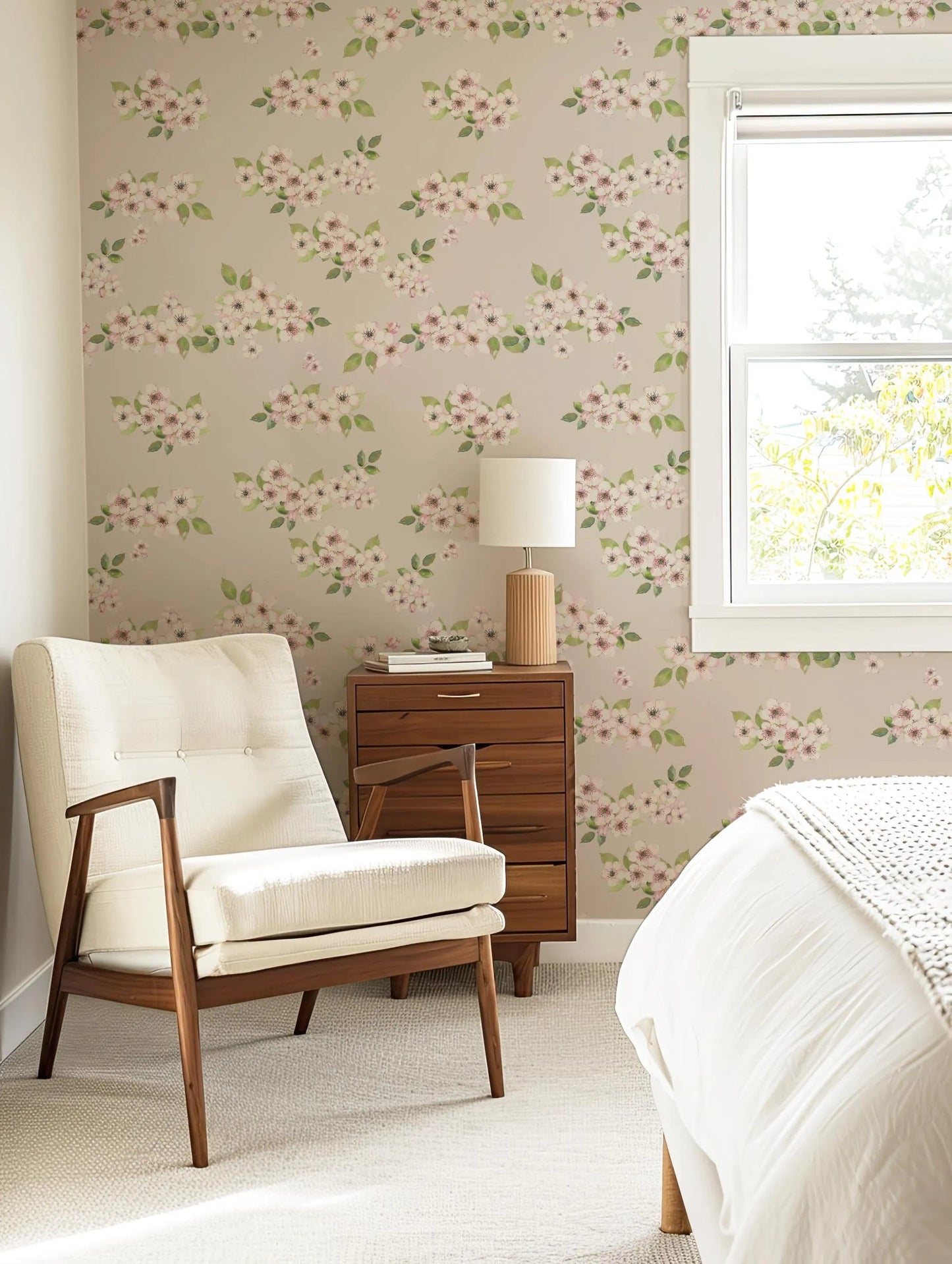 a cozy bedroom with a floral wallpaper, a white armchair, a wooden side table with a lamp, and a window with white blinds.