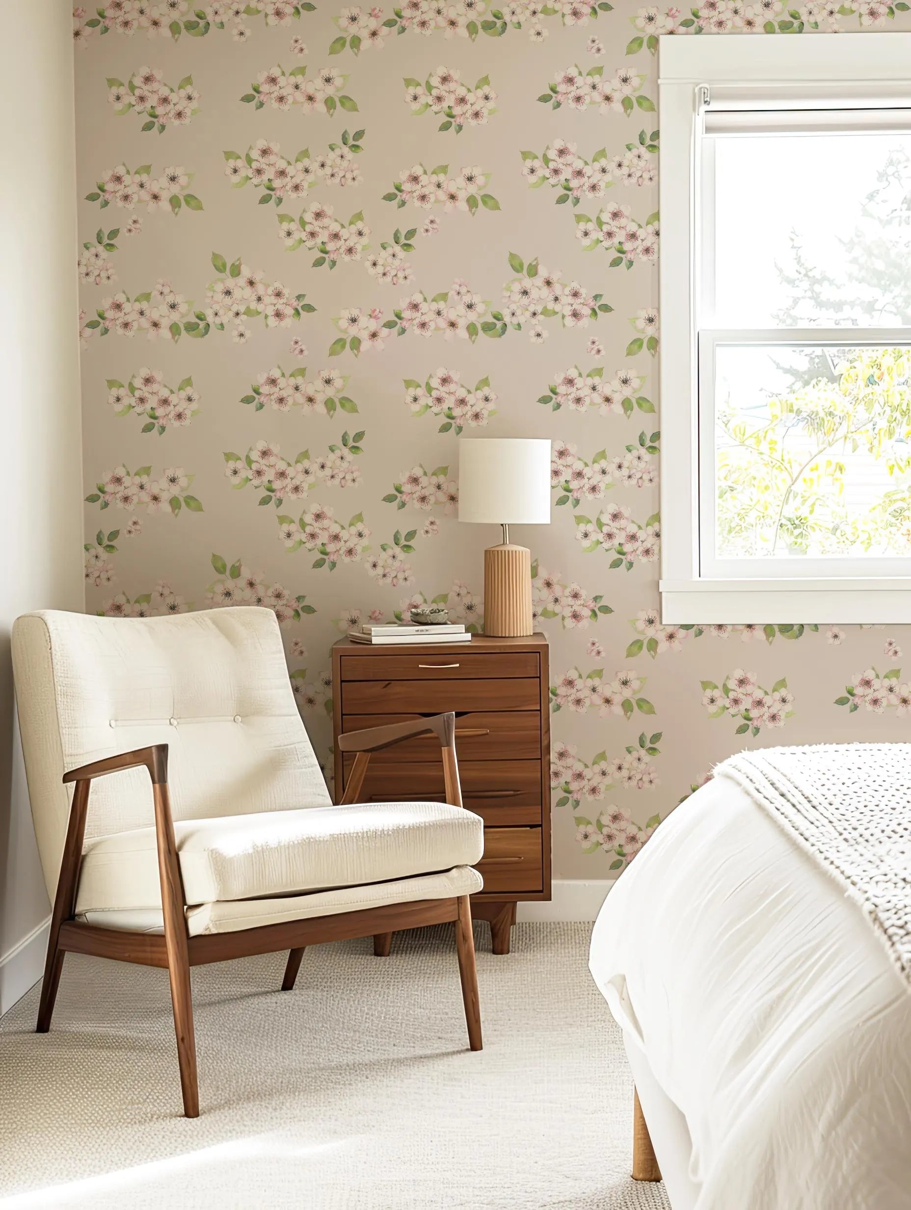 a cozy bedroom with a floral wallpaper, a white armchair, a wooden side table with a lamp, and a window with white blinds.