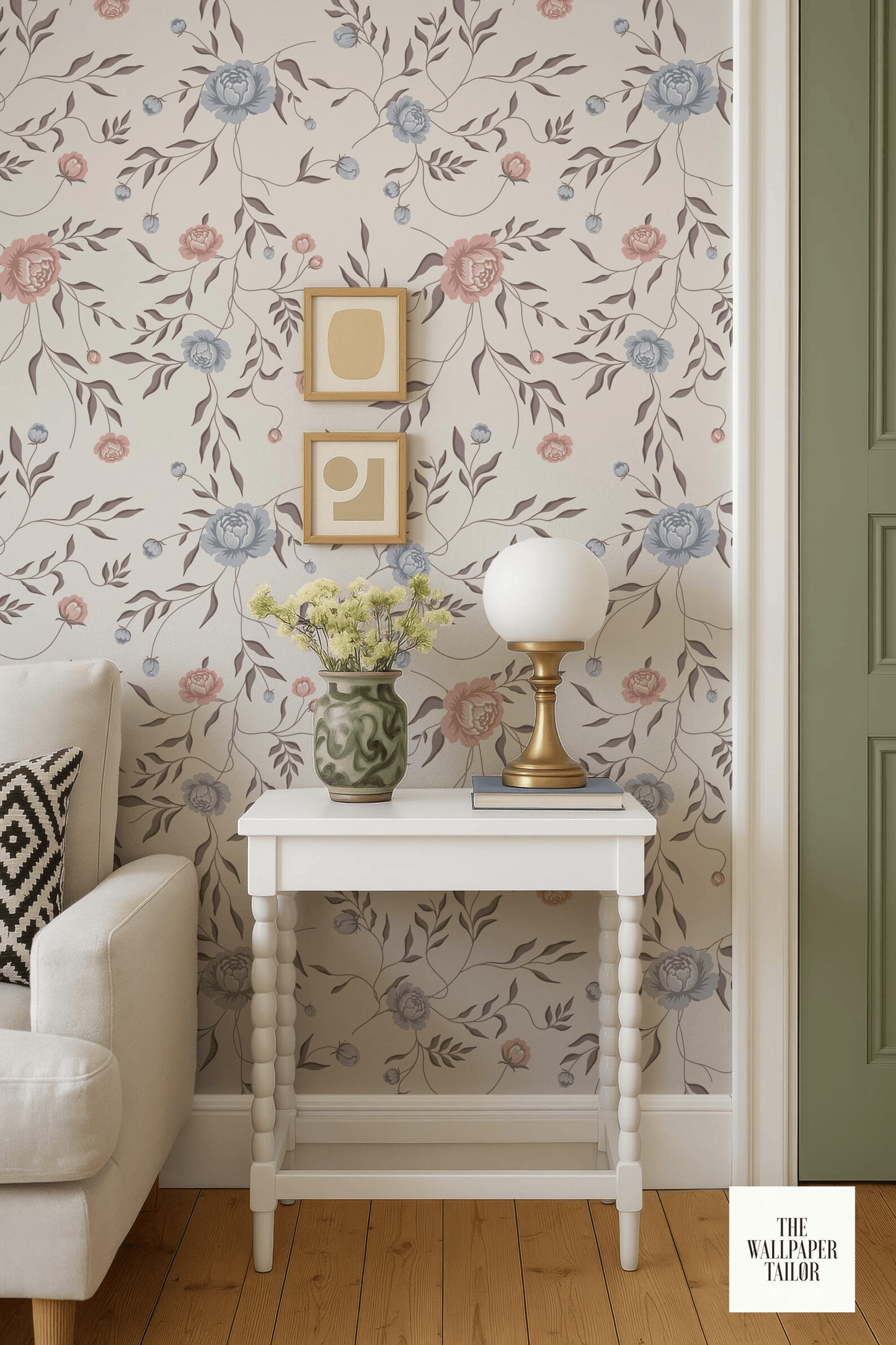 a cozy living room with a white sofa, a white side table with a lamp and a vase of flowers, and a floral wallpaper.