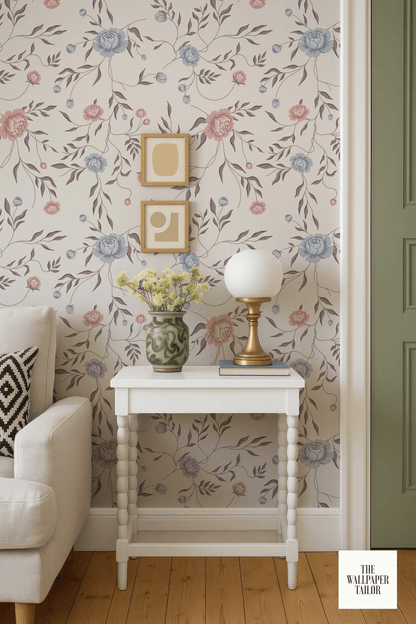 a cozy living room with a white sofa, a white side table with a lamp and a vase of flowers, and a floral wallpaper.