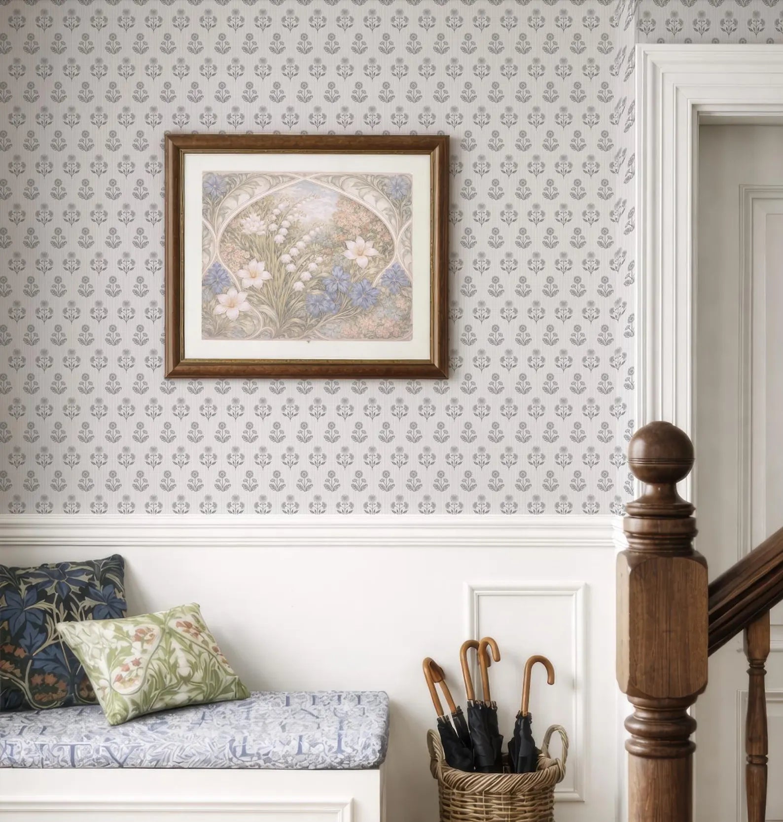a cozy and well-decorated room with a framed floral artwork hanging on the wall, a wooden staircase, a bench with pillows, and a basket of umbrellas.