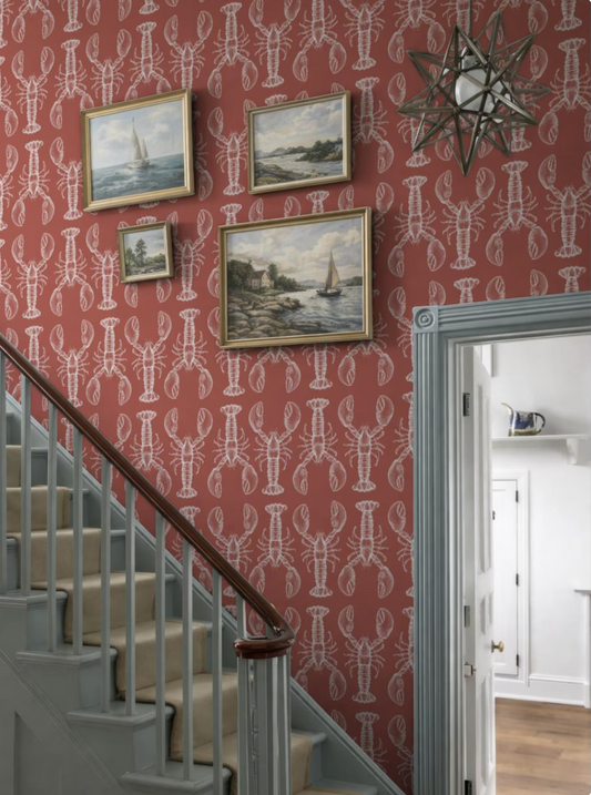 a staircase with a red and white patterned wallpaper, and three framed pictures of boats hanging on the wall above the staircase.