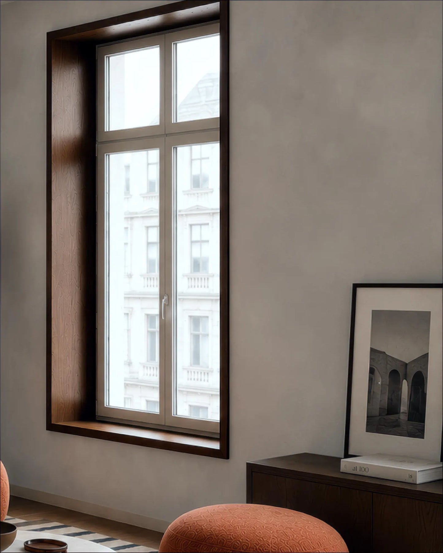 a cozy living room with a large window overlooking a cityscape, a wooden bookshelf, and a framed photograph on the wall.
