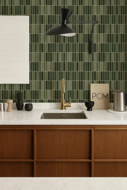 a modern kitchen with a white countertop, a gold faucet, and a wooden cabinet. The walls are covered in green and white tiles, and there is a black light fixture above the sink.