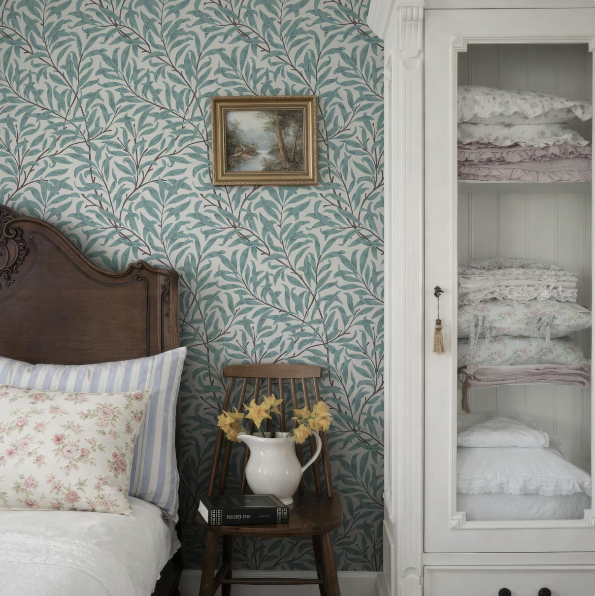 a cozy bedroom with a wooden headboard, a white and blue striped pillow, a white vase with yellow flowers, and a framed picture on the wall.