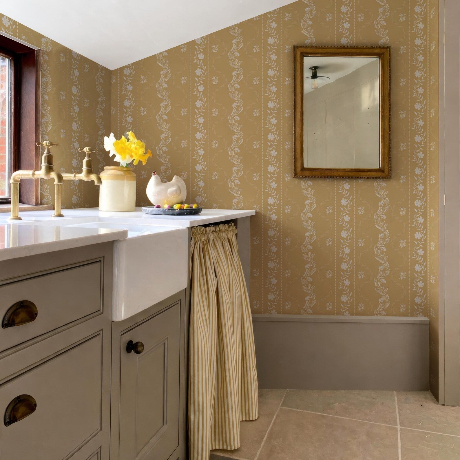 a bathroom with a sink, a mirror, and a window. The walls are covered in a floral wallpaper, and there is a curtain hanging from the window.