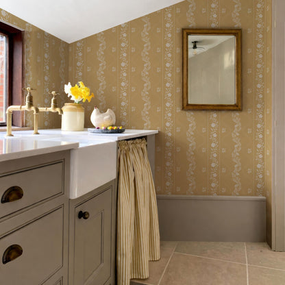 a bathroom with a sink, a mirror, and a window. The walls are covered in a floral wallpaper, and there is a curtain hanging from the window.