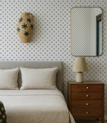 a bedroom with a bed, a mirror, and a wooden dresser. The bed has a gray headboard and white pillows. The mirror is mounted on the wall above the bed, and the dresser has a lamp on it. The wall has a patterned wallpaper with small white dots.