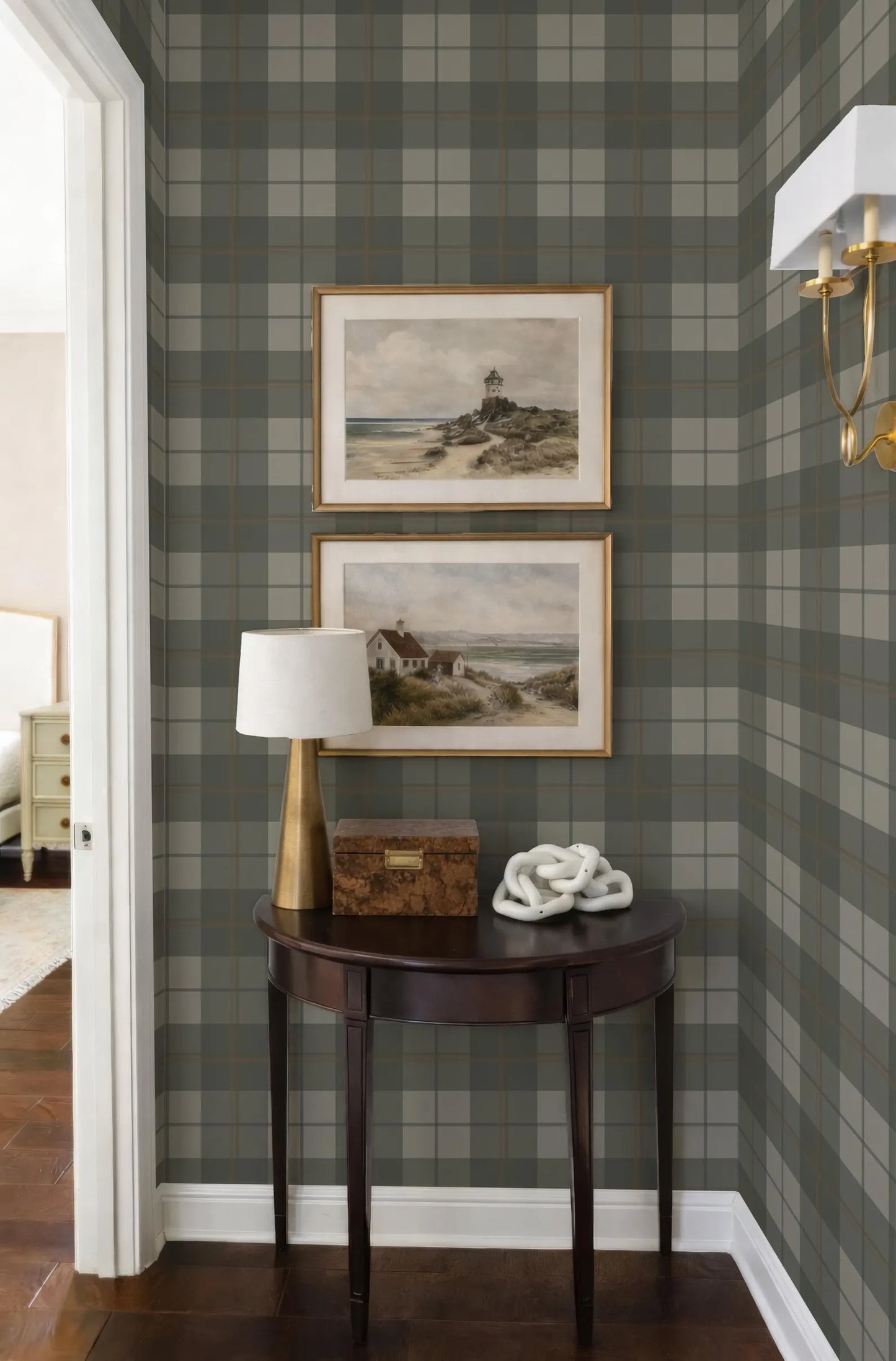 a corner of a room with a wooden table, a lamp, and two framed landscape paintings on the wall above it.