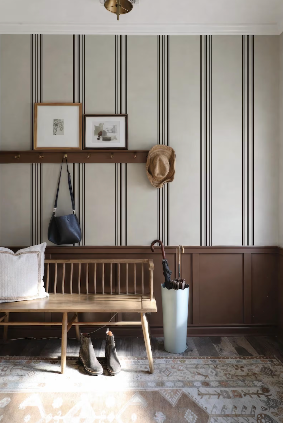 a cozy entryway with a wooden bench, a white umbrella, and a pair of boots. The walls are adorned with striped wallpaper, and there are two framed pictures hanging above the bench.