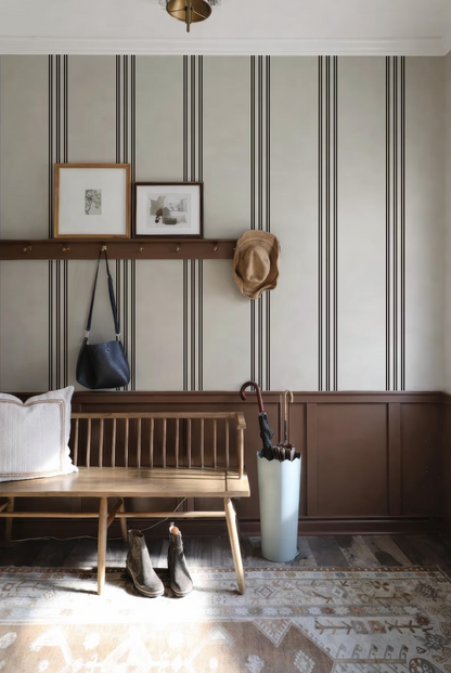 a cozy entryway with a wooden bench, a white umbrella, and a pair of boots. The walls are adorned with striped wallpaper, and there are two framed pictures hanging above the bench.