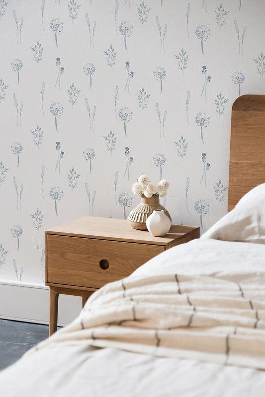 a bedroom setting with a wooden nightstand, a vase of flowers, and a patterned wallpaper.