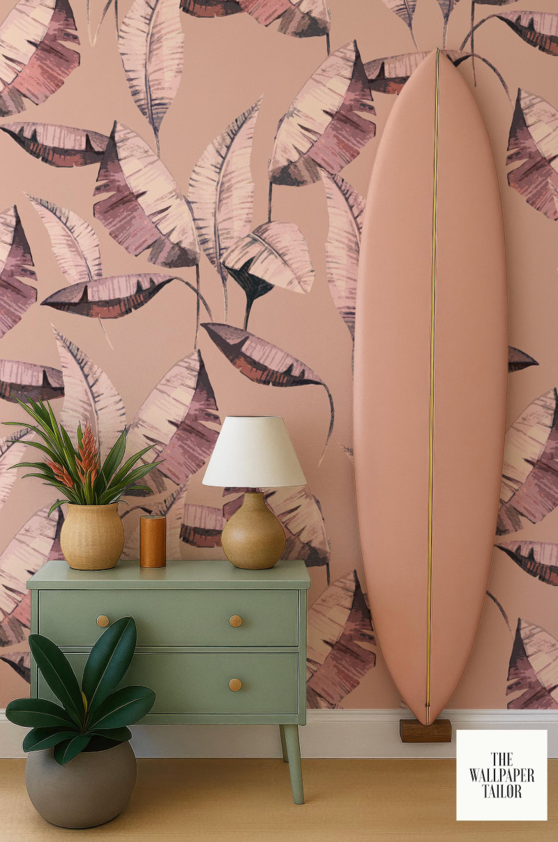 a vibrant pink wall with a large, colorful leaf pattern, a green dresser with a lamp, a potted plant, and a surfboard leaning against the wall.