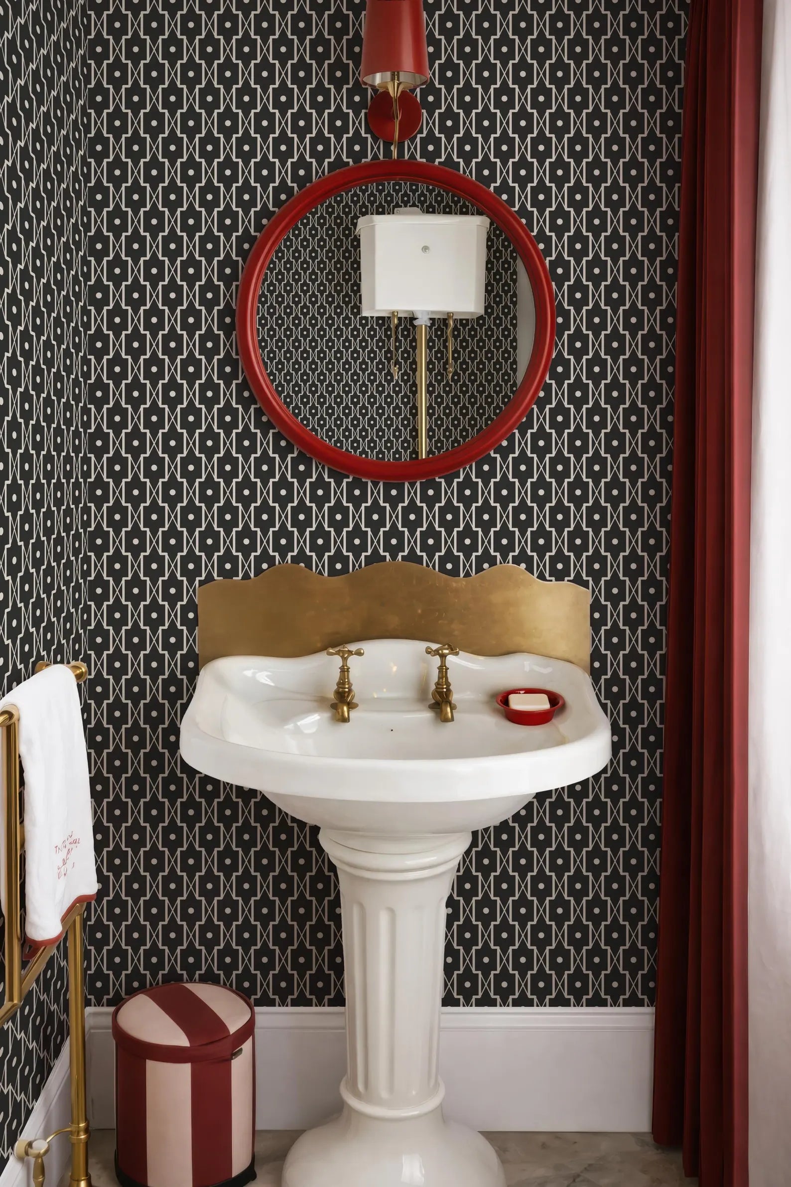 a bathroom with a white pedestal sink, a red and white striped stool, and a black and white patterned wallpaper.
