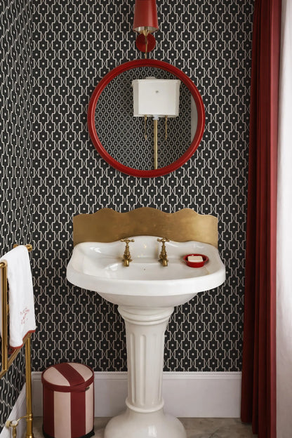 a bathroom with a white pedestal sink, a red and white striped stool, and a black and white patterned wallpaper.