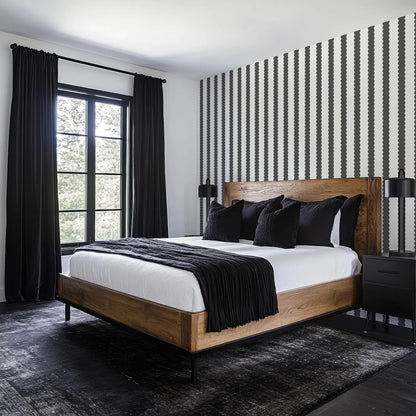 a modern bedroom with a large bed, wooden headboard, and black and white striped wallpaper. The bed is dressed in black bedding and has a wooden nightstand on each side. The room has a large window with black curtains, and the floor is covered in a gray rug.