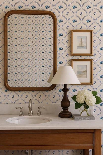 a bathroom vanity with a white sink, a mirror, a lamp, and a framed picture of a sailboat. The wall behind the vanity has a blue and white floral pattern.