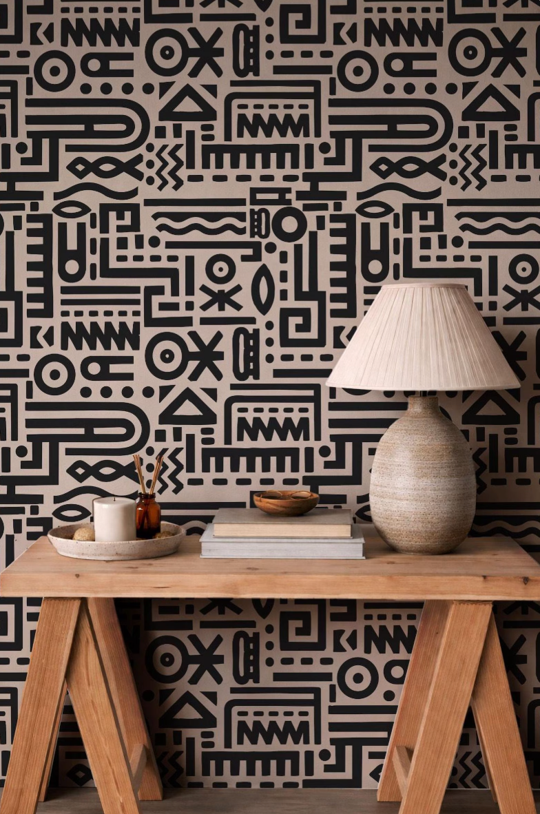 a wooden table with a lamp, a stack of books, and a small bowl on it, set against a wall with a black and white abstract pattern.