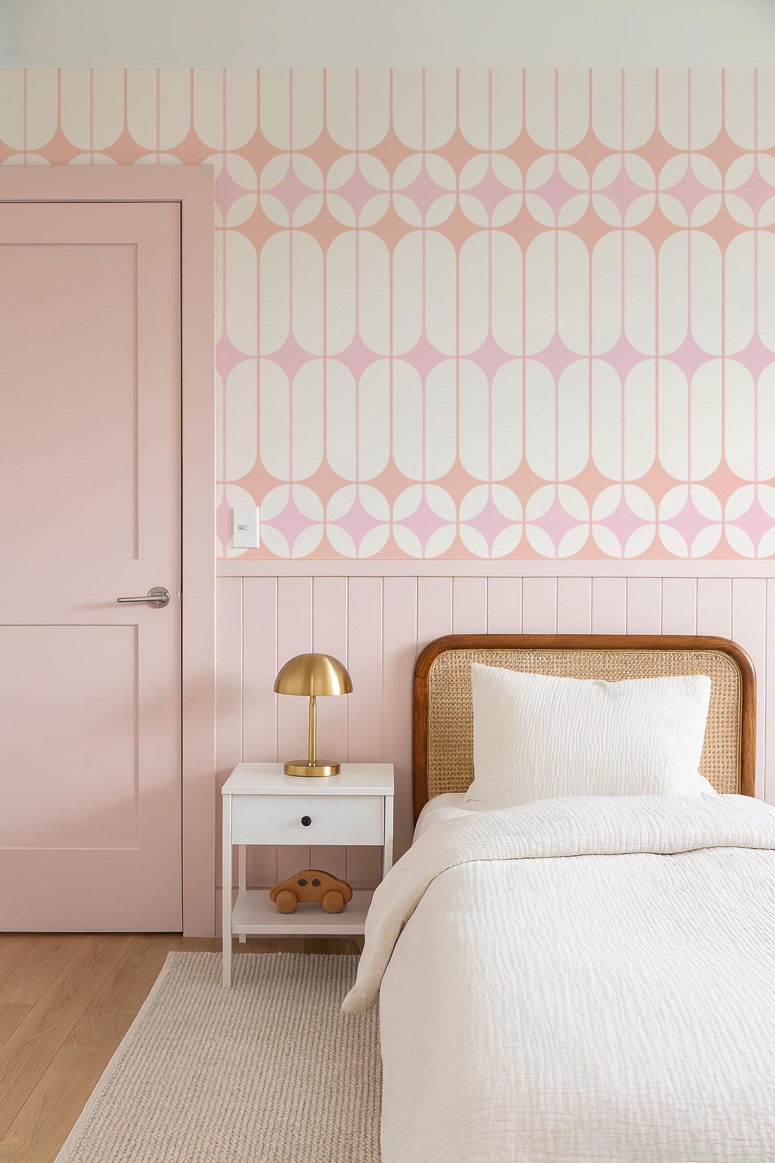 a bedroom with a pink door, a white bed with a wooden headboard, and a white nightstand with a lamp. The walls are decorated with a geometric pattern in shades of pink and white.