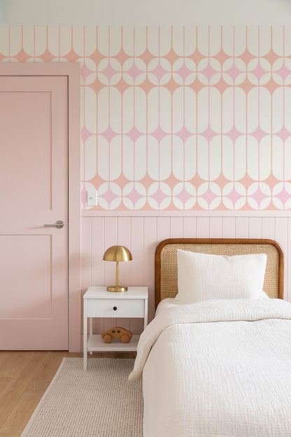 a bedroom with a pink door, a white bed with a wooden headboard, and a white nightstand with a lamp. The walls are decorated with a geometric pattern in shades of pink and white.