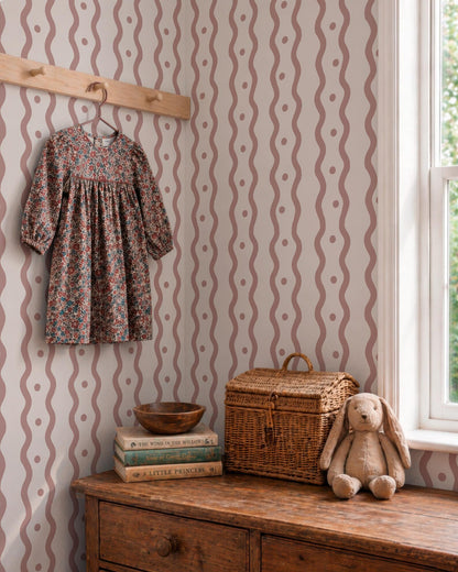 a dress hanging on a wooden hanger, a stack of books, a wicker basket, and a stuffed rabbit on a wooden dresser.