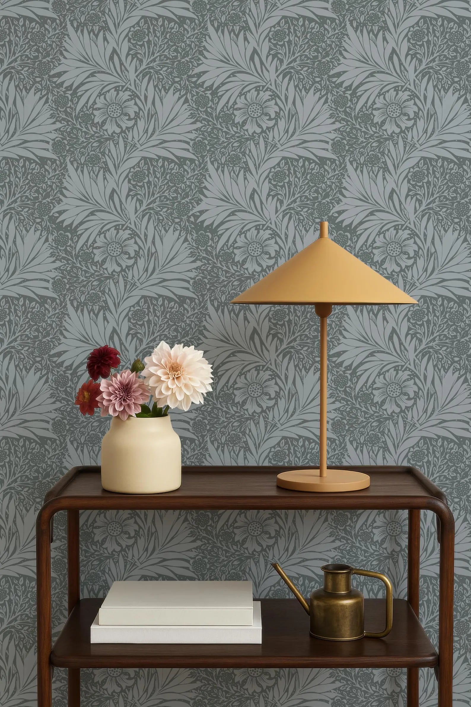a wooden side table with a lamp, a vase with flowers, and a book on it. The table is set against a gray and white patterned wallpaper.