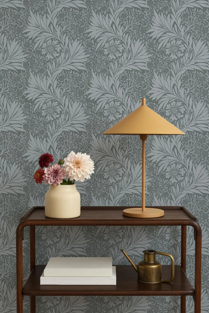 a wooden side table with a lamp, a vase with flowers, and a book on it. The table is set against a gray and white patterned wallpaper.