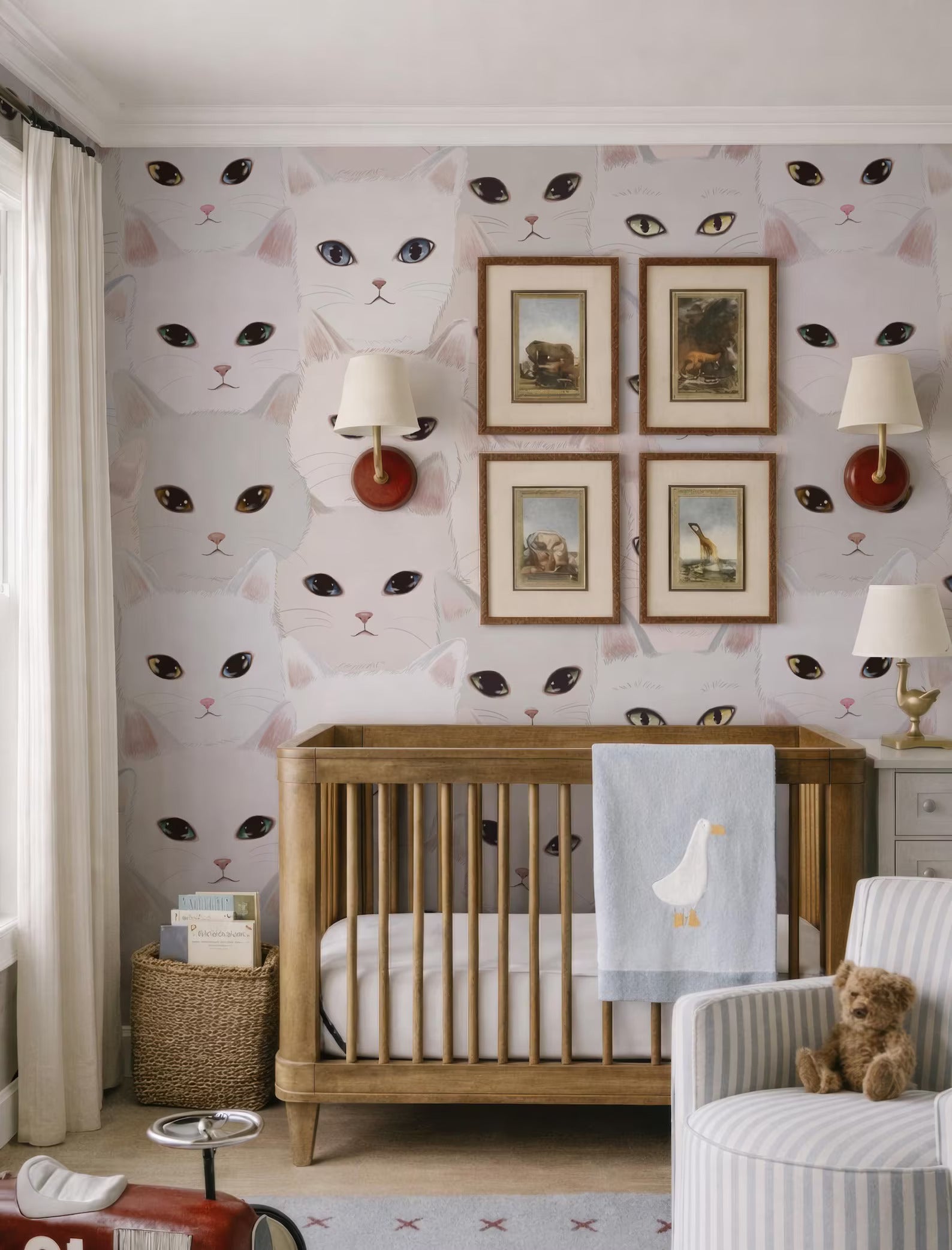 a nursery room with a wooden crib, a teddy bear, and a wallpapered wall with cat faces.