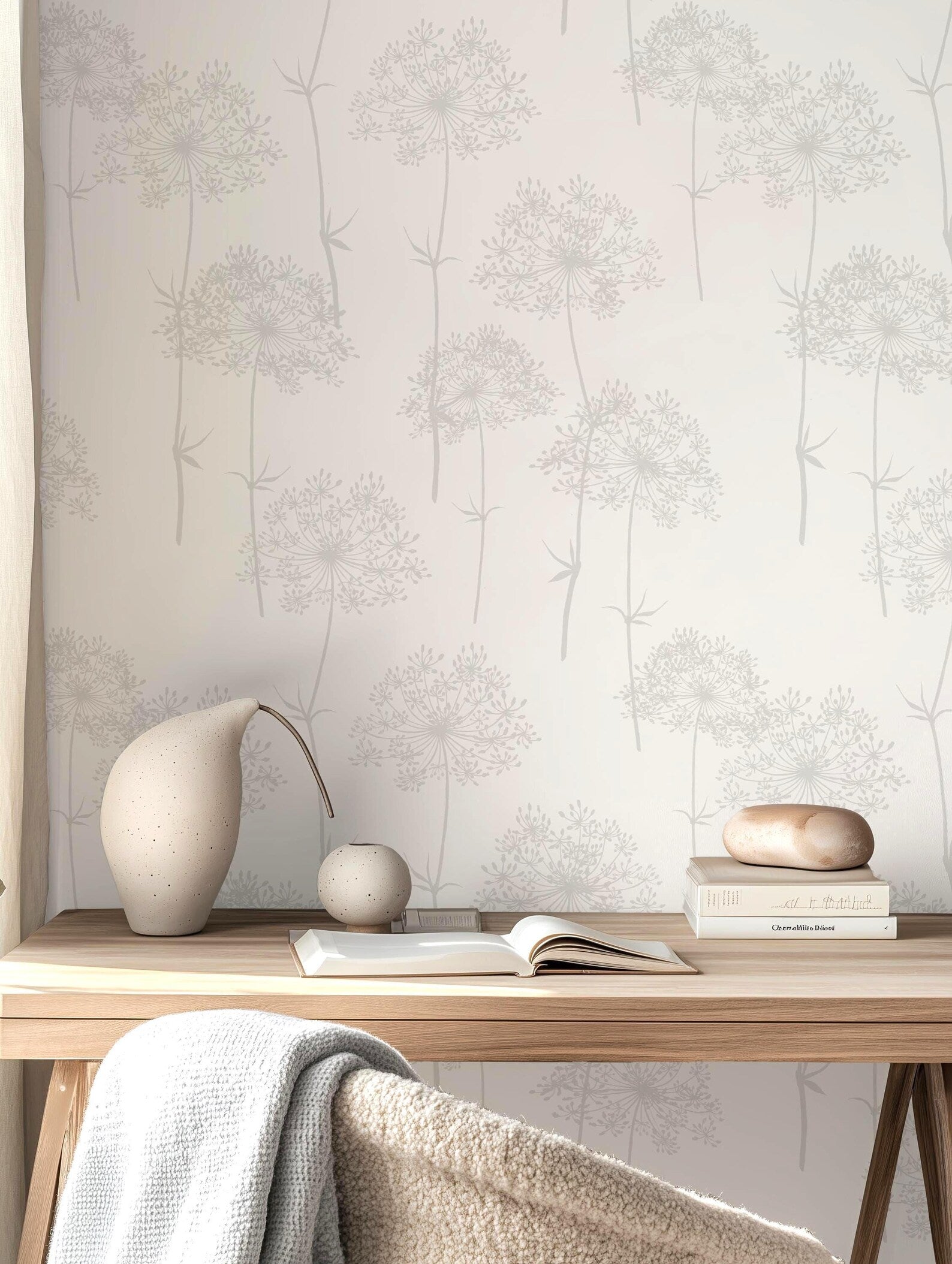 a wooden desk with a white vase, a stack of books, and a small white figurine on it. The desk is situated against a wall with a patterned wallpaper.
