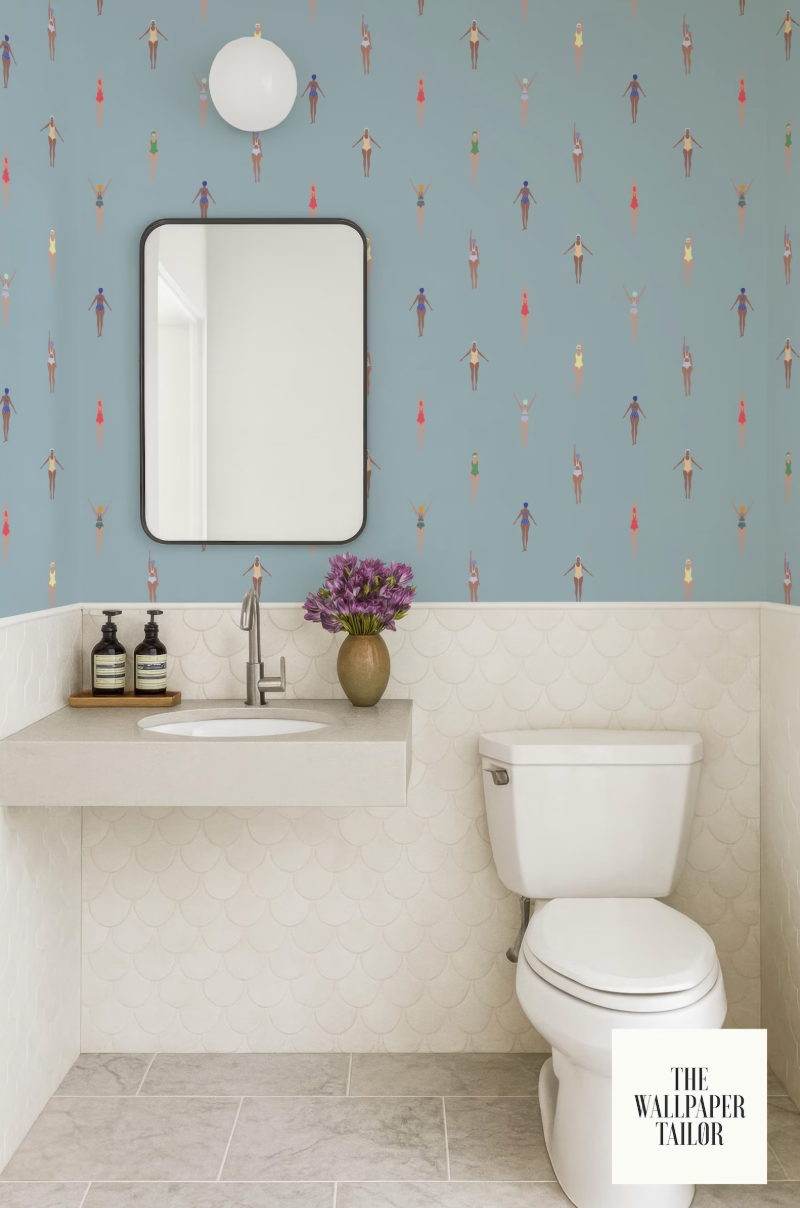 a bathroom with a white toilet, a sink with a mirror above it, and a blue wall with a pattern of small figures. There is also a vase of flowers on the sink.