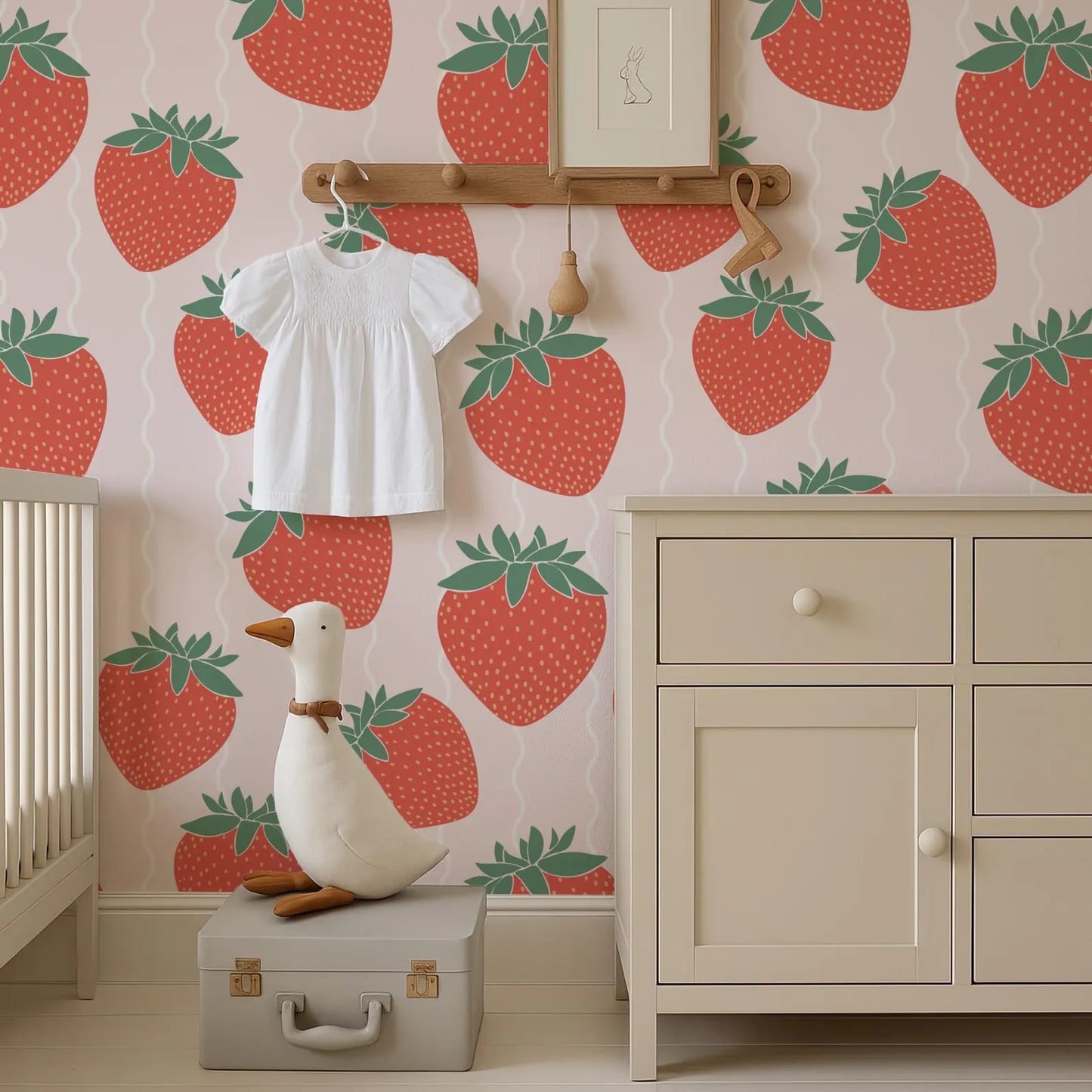 a nursery room with a white dresser, a stuffed duck, and a wallpapered wall with a strawberry pattern.